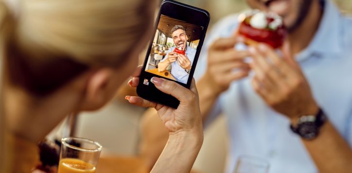 closeup-woman-taking-picture-her-boyfriend-who-is-eating-donut-cafe_resized-2